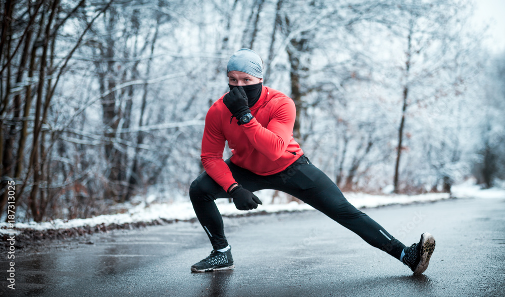 冬季跑步锻炼，雪地森林中的跑步者在路上伸展身体