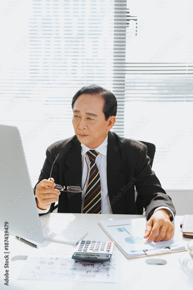 亚洲资深金融商人坐在电脑前的工作站上。