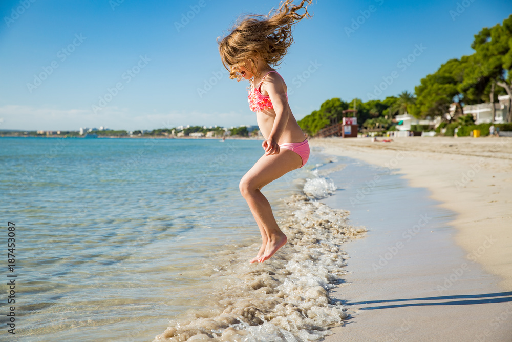 可爱快乐的小女孩穿着泳衣在海滩上奔跑，跳过海浪。美丽的相扑