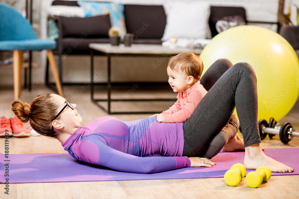 穿着运动服的年轻母亲和她顽皮的小儿子躺在家里的垫子上锻炼