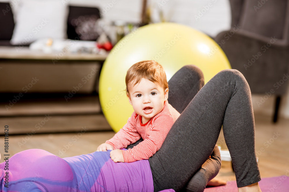 一个可爱顽皮的男婴和她的母亲穿着运动服在家锻炼的肖像