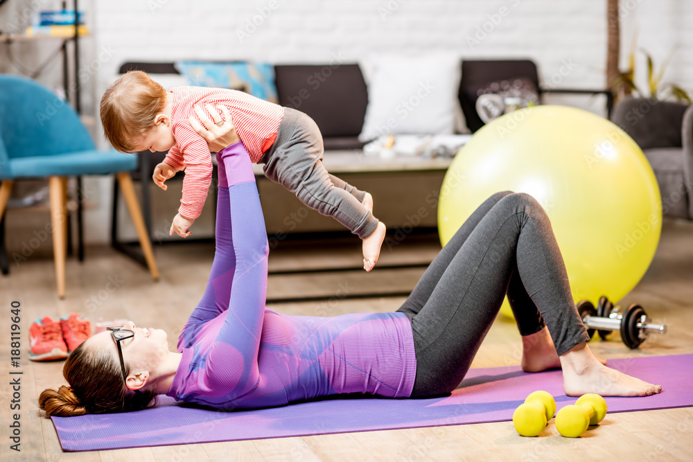 穿着运动服的年轻母亲在家里的垫子上抱着她的小儿子做运动