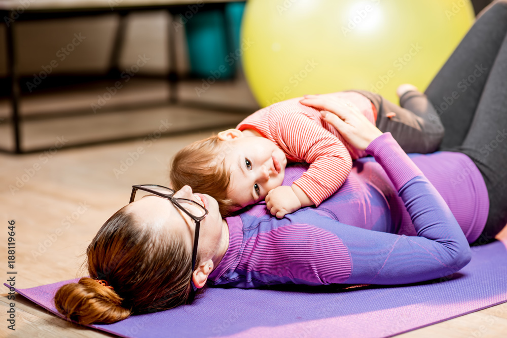 一位穿着运动服的年轻母亲和她的男婴在家锻炼后躺着放松的画像