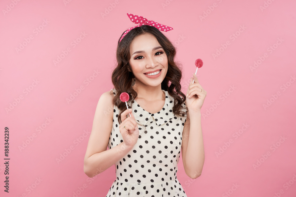 时尚的亚洲女人拿着棒棒糖，在粉色背景下摆姿势