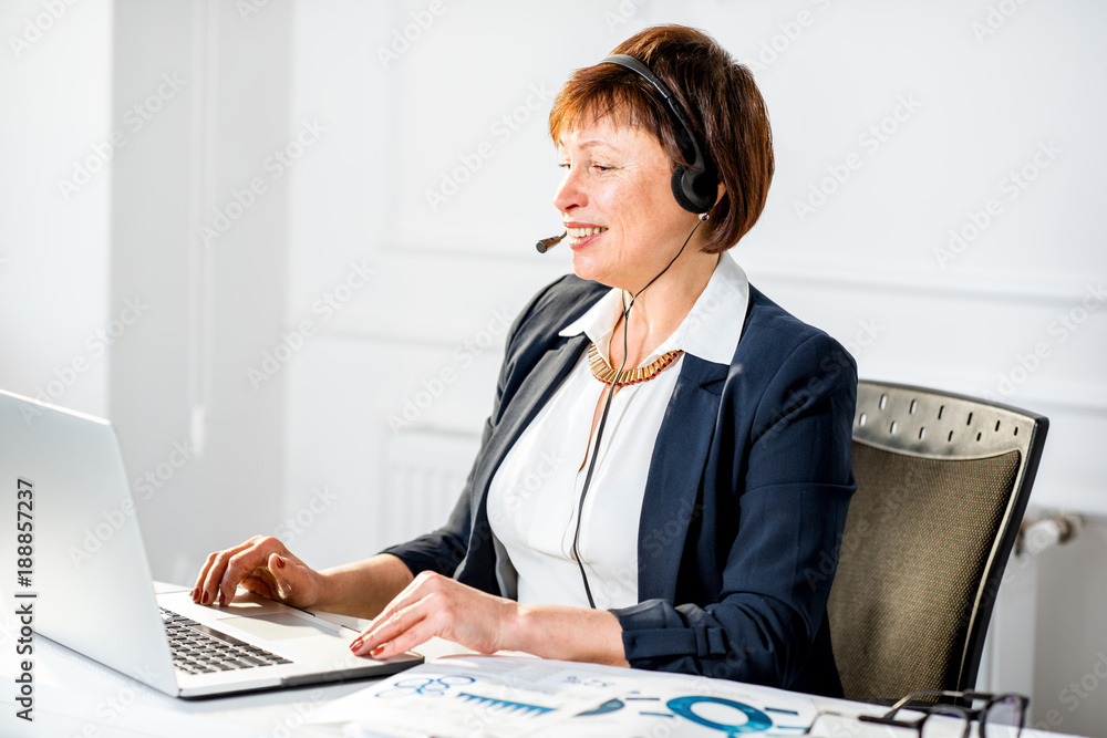 优雅的高级女商人在办公室戴着耳机在线工作