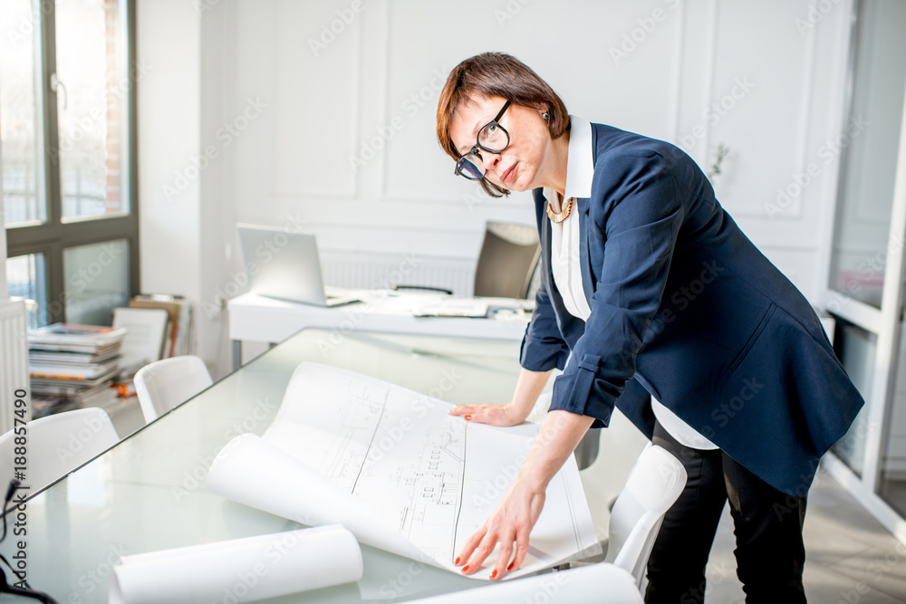 优雅的资深女建筑师站在白色办公室里处理图纸