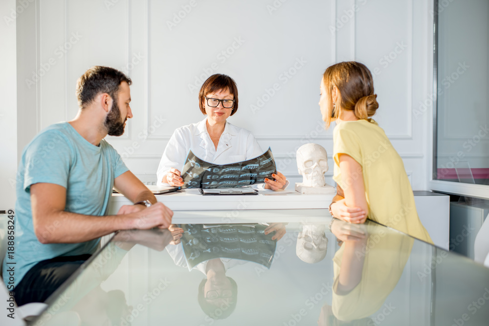 Young couple having a consultation with senior doctor discussing x-ray print sitting in the white of