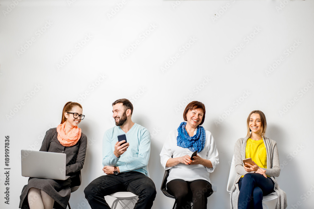 人们穿着五颜六色的休闲服，在白墙背景上坐成一排使用小工具