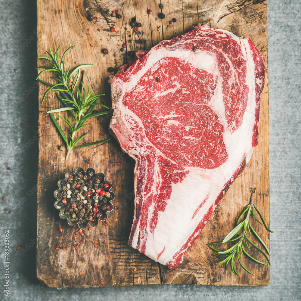 生优质牛肉、干熟牛排、肋眼贴骨，铺在灰色co上的乡村木板上