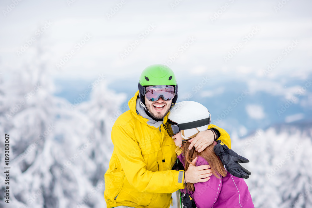 一对穿着单板滑雪服的年轻夫妇在雪山上度过寒假，玩得很开心