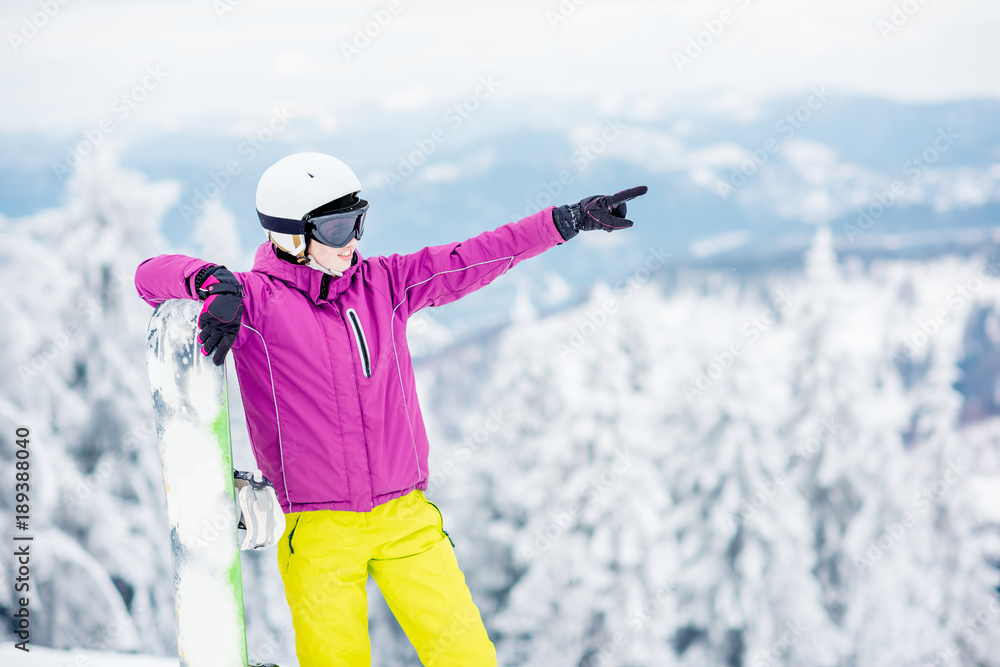 一位年轻的单板滑雪女运动员站在户外雪山上用手指着的肖像