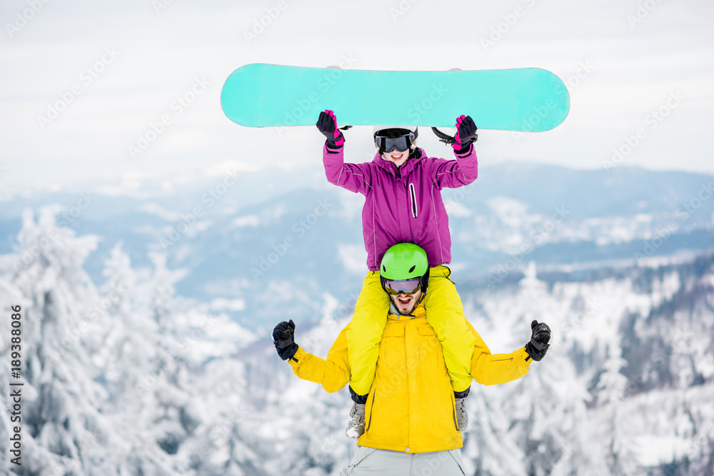 一对穿着滑雪服的年轻夫妇在雪山上度过寒假，玩得很开心