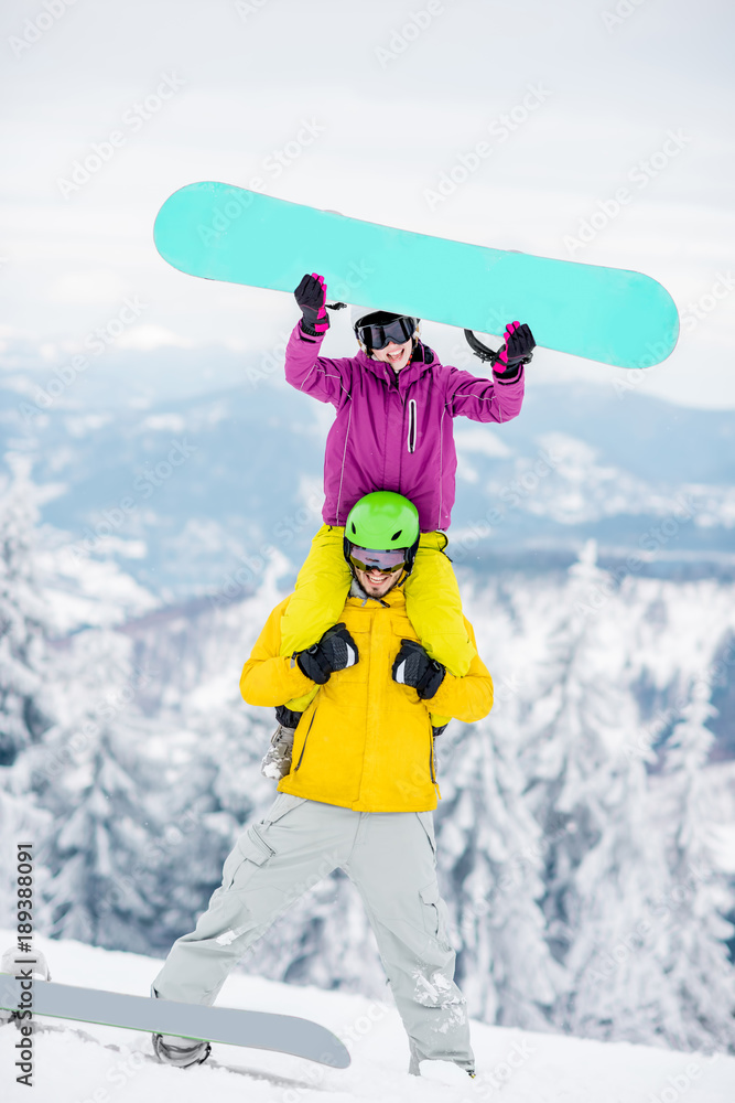 一对穿着滑雪服的年轻夫妇在雪山上度过寒假，玩得很开心