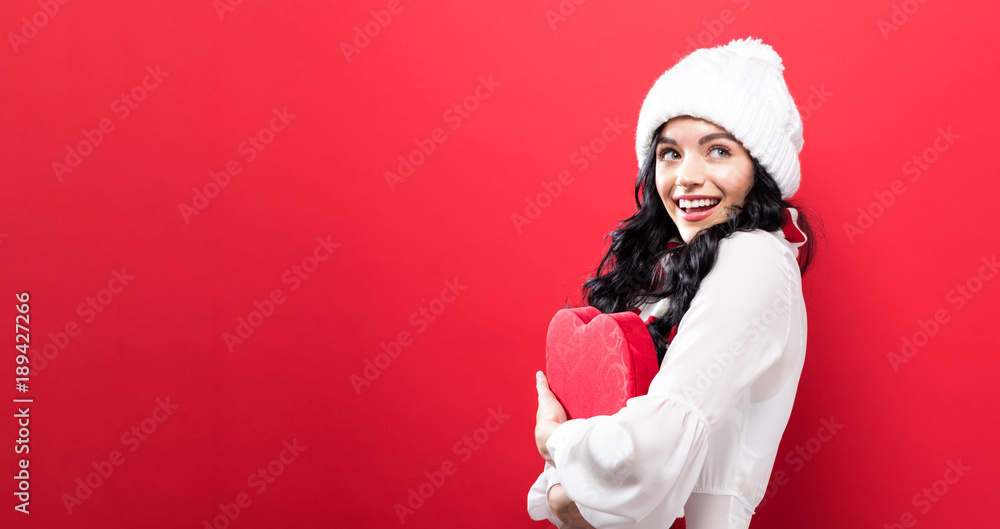 快乐的年轻女人在坚实的背景上拿着一个大大的爱心礼盒