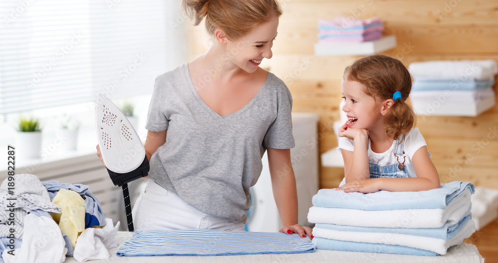 幸福的家庭母亲家庭主妇和孩子女儿在洗衣房熨衣服