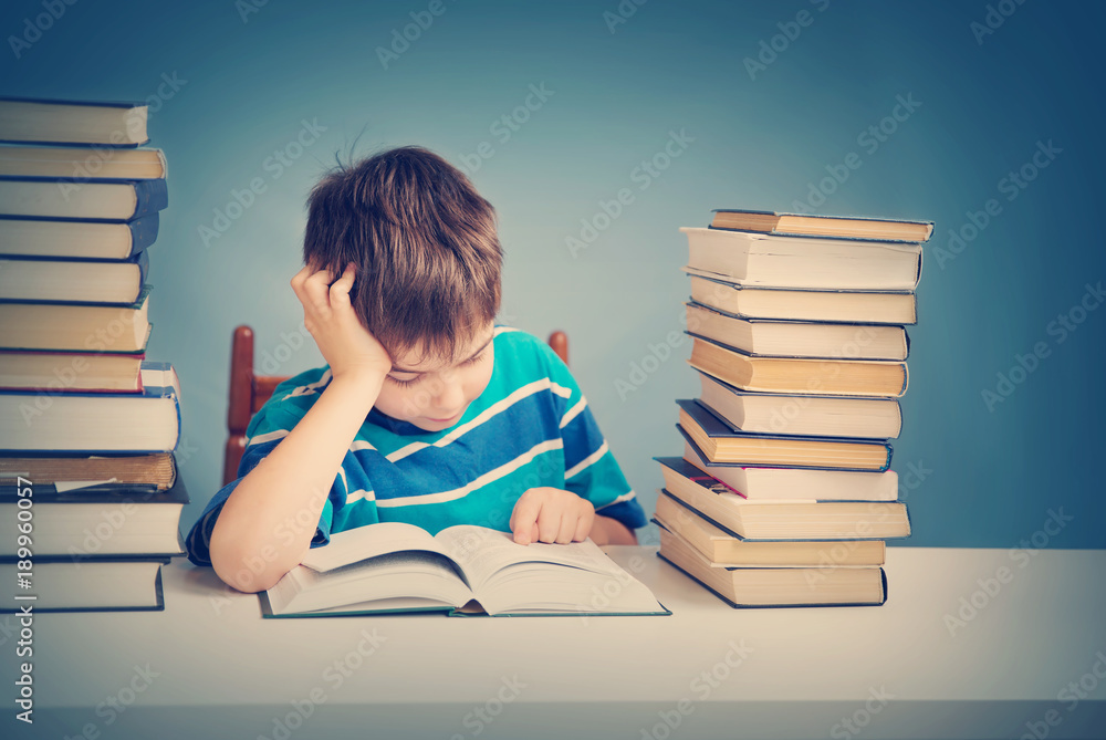 seven years old child reading a book at home. Boy studing at table on blue background