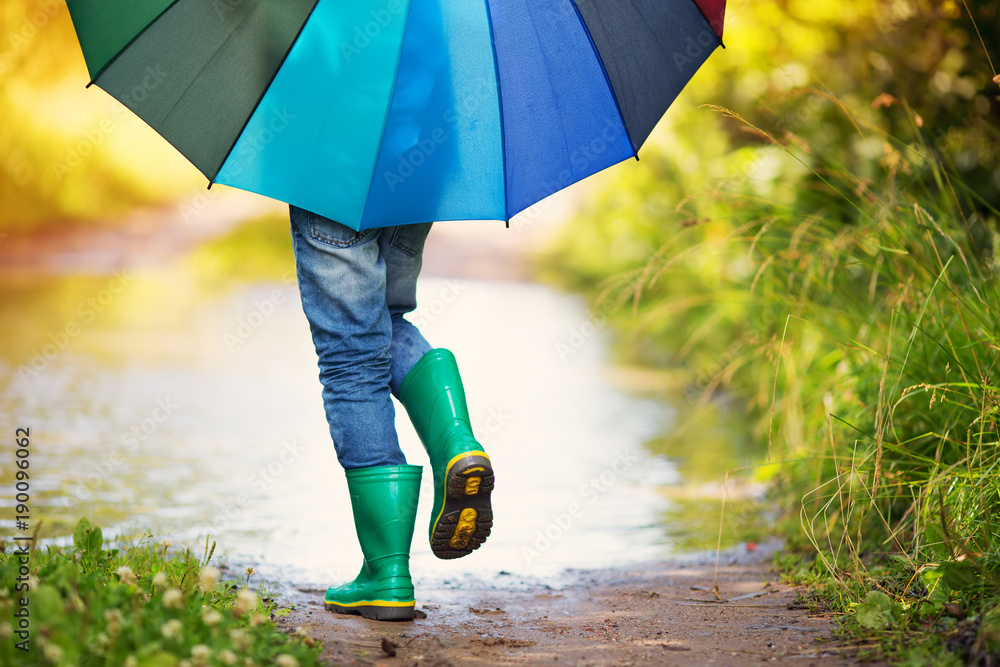 雨天，孩子穿着雨鞋在水坑里行走。苏州，男孩在雨中撑着五颜六色的伞
