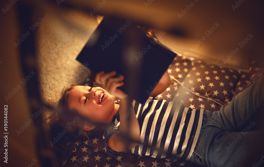 快乐的小女孩在家里的帐篷里在黑暗中笑着看书