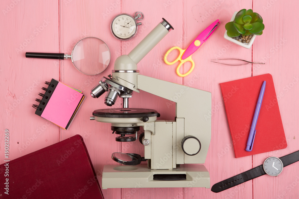 Education concept - notepad, microscope on the pink wooden desk