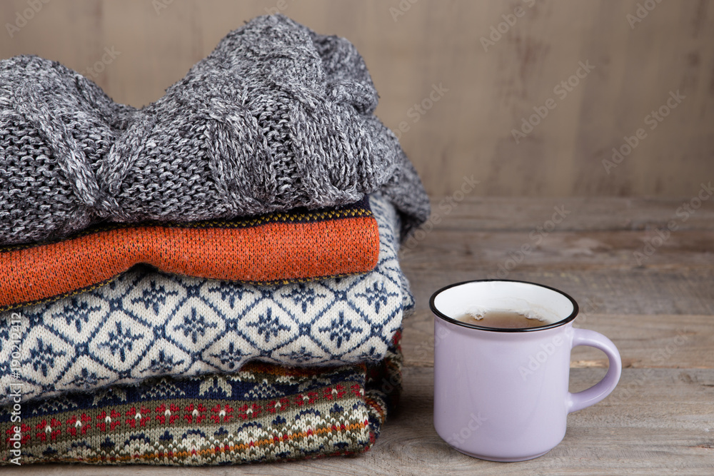 一堆针织的冬季毛衣和一杯木制背景的茶