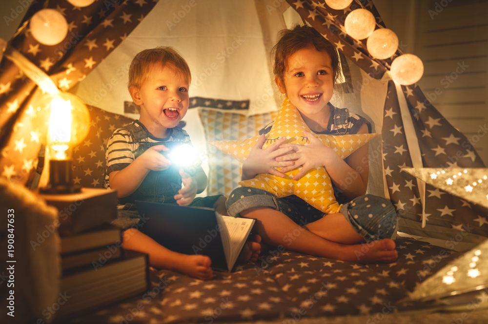 帐篷里带着手电筒看书的儿童男孩和女孩