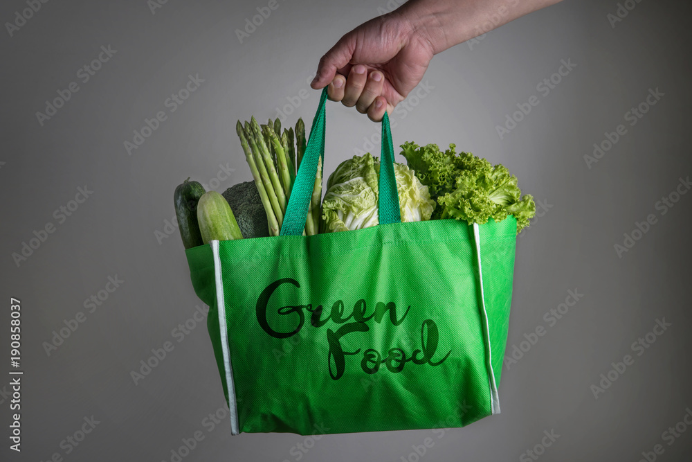 合上一个手持绿色食品袋，里面有混合有机绿色蔬菜的绿色食品文本，