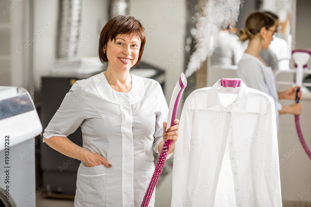 一位穿着制服的资深洗衣女工在教授办公室用蒸汽机熨白衬衫的肖像