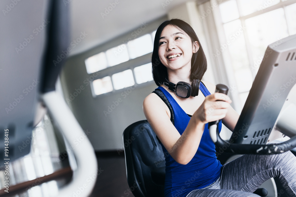 漂亮聪明的亚洲运动女性戴着耳机在跑步机上跑步用h听音乐