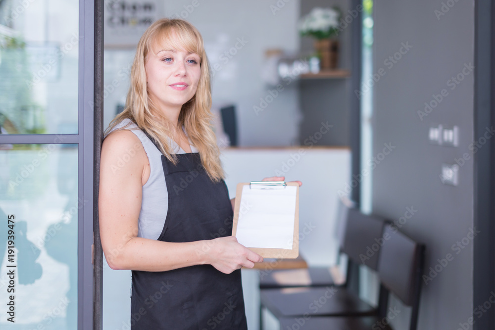 企业主高加索女人拿着菜单上的围裙，围裙上有咖啡店的背景