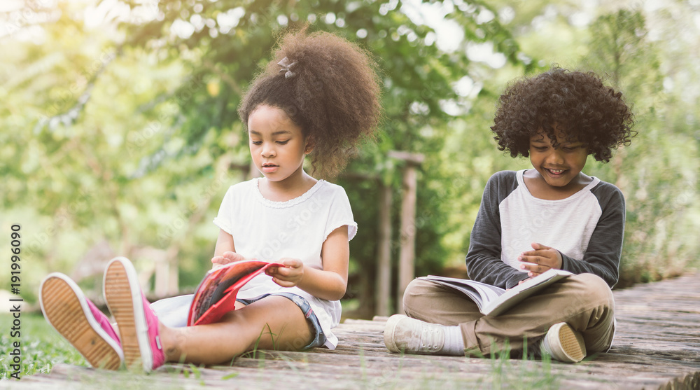 非洲小女孩与朋友在绿色尖刺之间的草地花园读书，阅读教育c