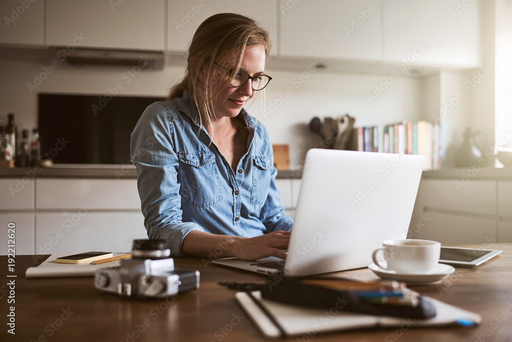 年轻女子在厨房里拿着笔记本电脑上网工作