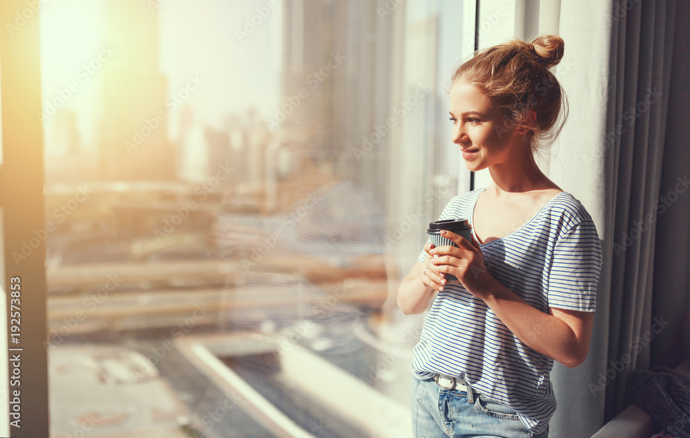 快乐的年轻女人早上在窗口喝咖啡