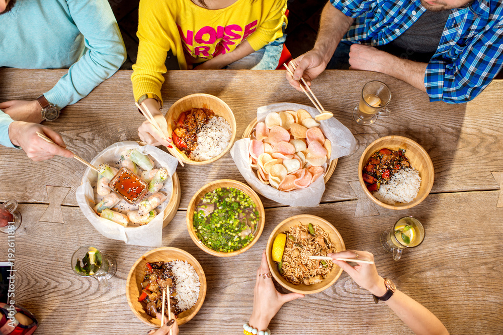 餐桌上的俯视图，桌上摆满了装在木板里的不同亚洲饭菜，年轻人在吃
