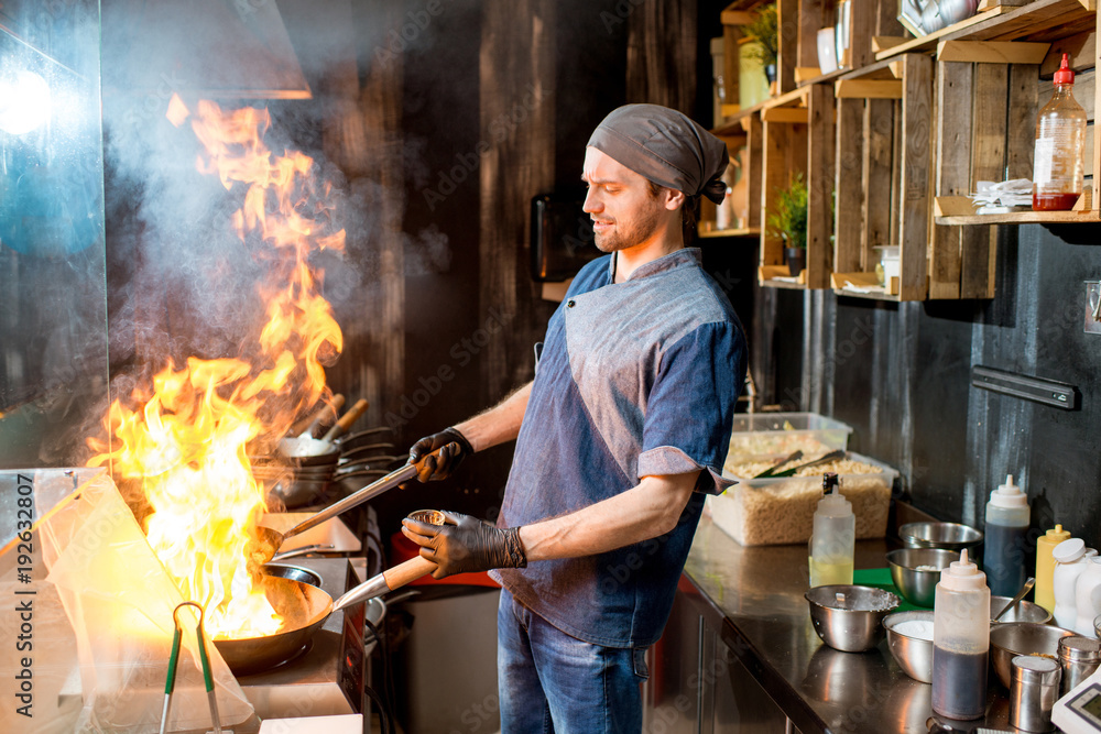 高加索首席厨师在亚洲餐厅的厨房里用火烈鸟在炒锅上烹饪