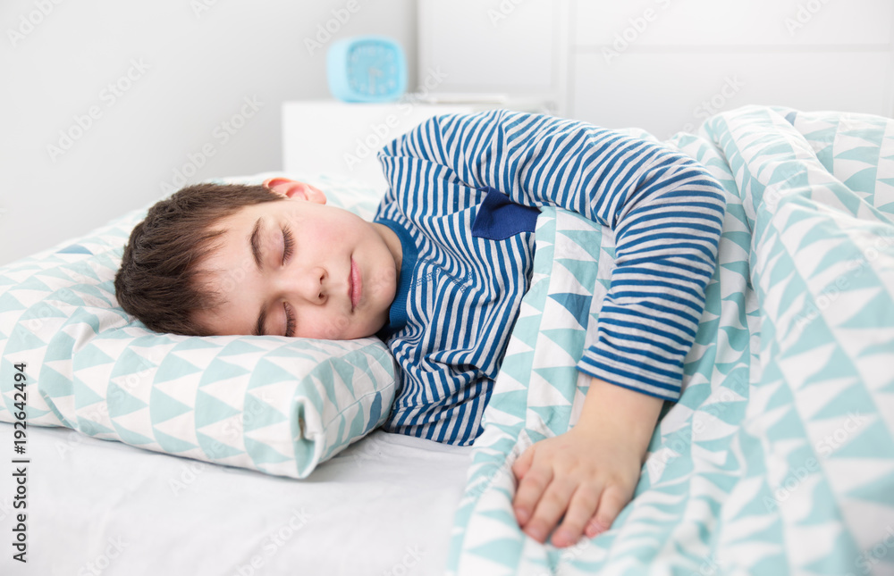 八岁的孩子睡在床上的枕头上。男孩睡在白色卧室里