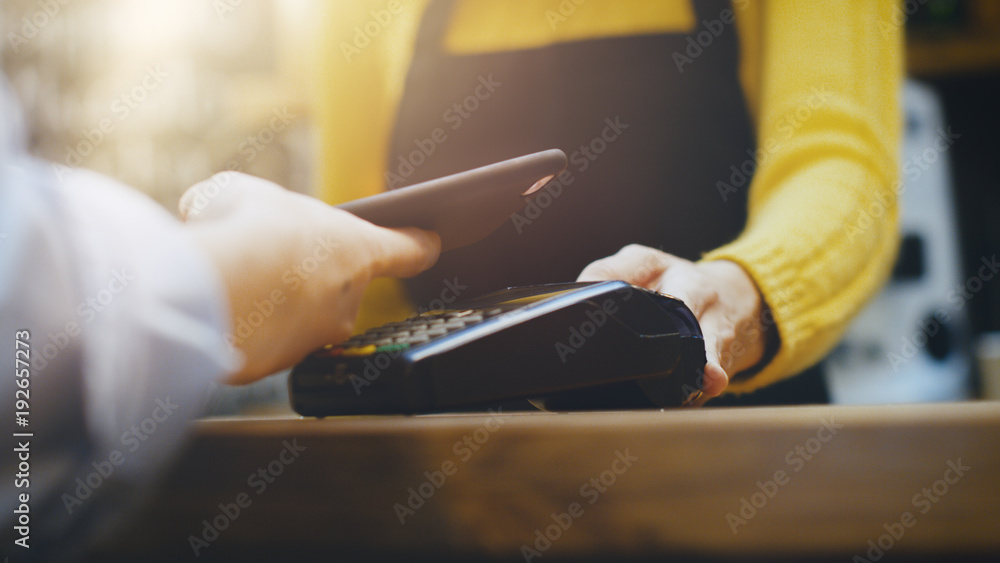 咖啡馆工作人员向使用非接触式手机支付信用卡的顾客销售外卖咖啡