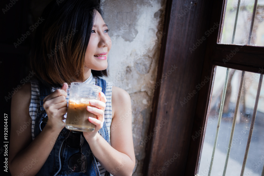 亚洲女性在临近窗口的早晨喝着热饮咖啡