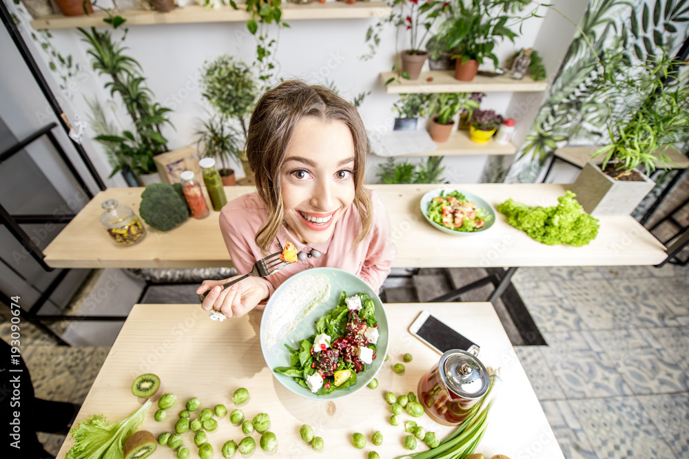 年轻女子坐在美丽的室内，背景是绿色的花朵，手里拿着健康的食物