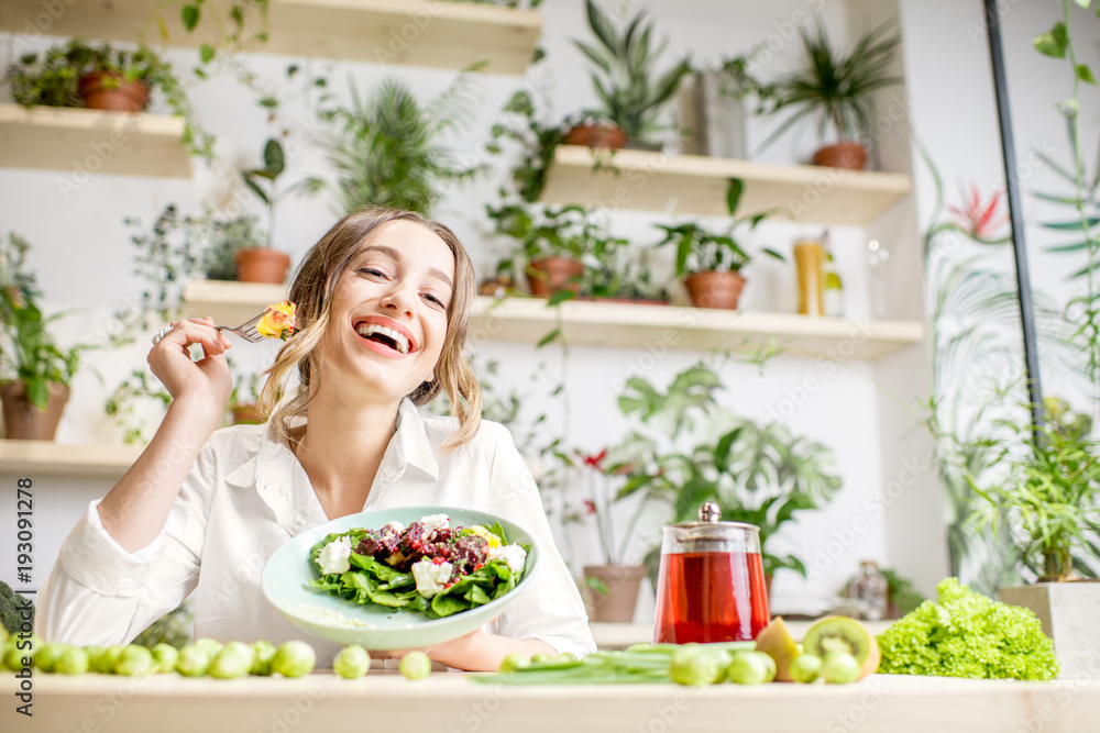 年轻女子坐在美丽的室内吃健康食品，背后开着绿色的花朵