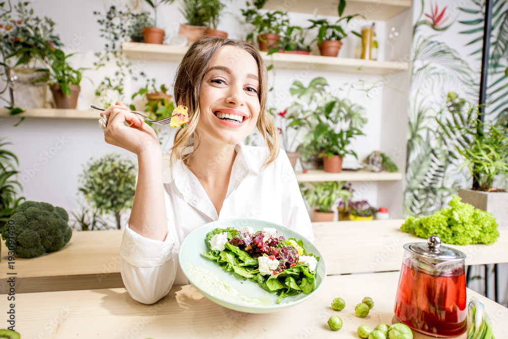 一位年轻女性坐在开着绿色花朵的美丽室内，吃着健康食品的肖像o
