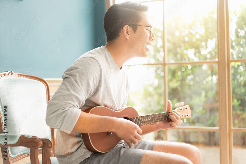 亚洲年轻人在家弹原声吉他尤克里里琴。享受原声吉他sunshin