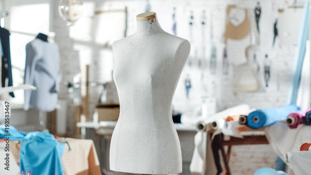 一个站在阳光明媚的工作室里的裁缝模特的照片。各种缝纫物品和服装