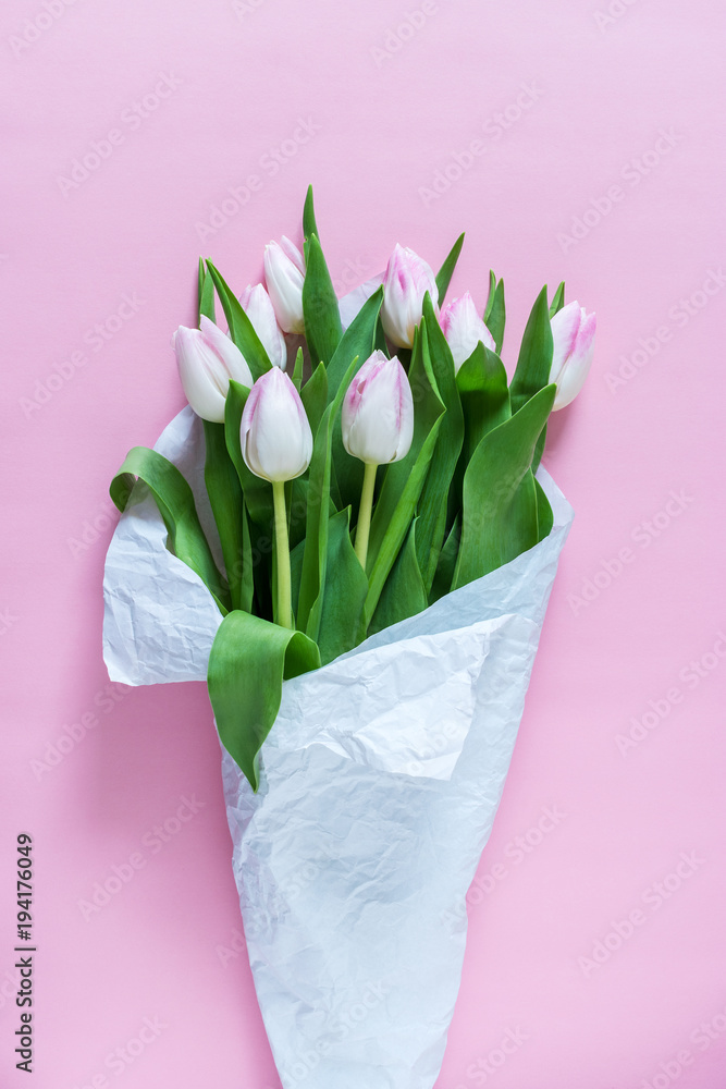 粉红色的郁金香用白色的纸包裹在粉红色的背景上。平躺。爱情的概念。