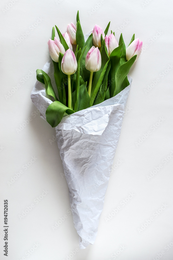 白色背景上用白纸包裹的粉红色郁金香。平躺。爱情概念。
