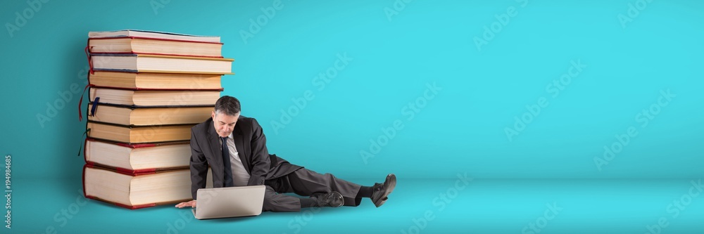 Business man using computer on the floor next to a pile of books