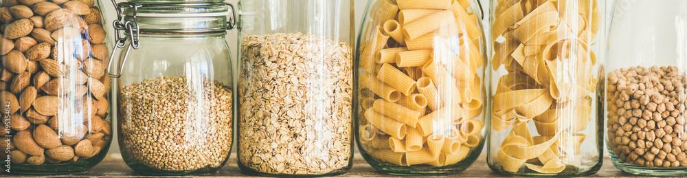 在木桌上的玻璃罐中进行健康烹饪的各种未煮熟的谷物、谷物、豆类和意大利面，