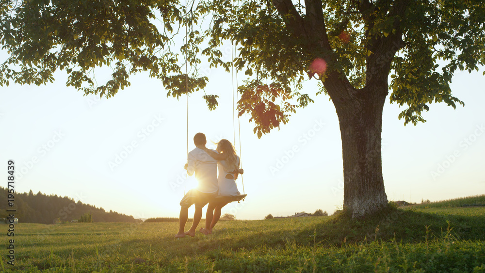 LENS FLARE SILHOUTE：金色黄昏，一对可爱的年轻情侣坐在秋千上