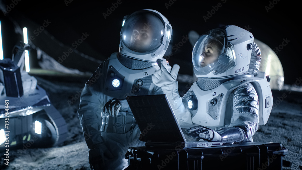 两名宇航员穿着太空服在笔记本电脑上工作，探索新发现的行星，发送通信