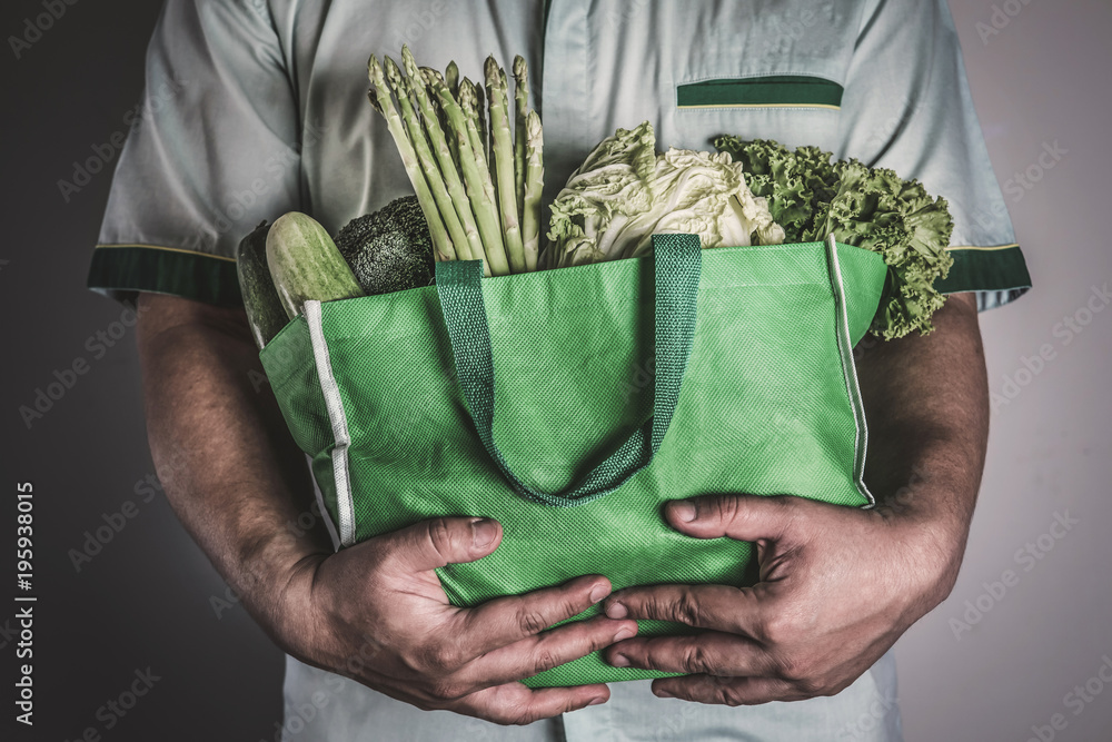合上一个手拿绿色食品袋，里面装着混合的有机绿色蔬菜，健康的有机gr