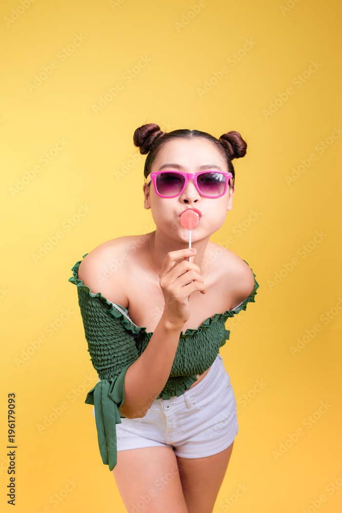 迷人时尚的年轻美女模特，红唇黄色背景，手里拿着糖果。
